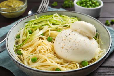 Photo of Bowl of delicious pasta with burrata, peas and zucchini on wooden table, closeup