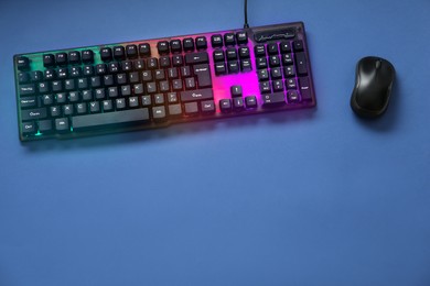 Modern RGB keyboard and mouse on blue background, flat lay. Space for text