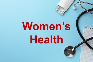 Words Women's Health, notebook, stethoscope and pills on light blue background, flat lay. Space for text