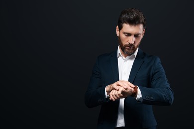 Handsome bearded man looking at wristwatch on black background. Space for text