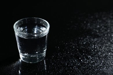 Glass of vodka on black wet table, space for text