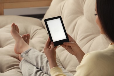 Young woman using e-book reader on sofa at home, closeup