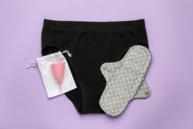 Women's underwear, reusable cloth pad and menstrual cup on violet background, top view