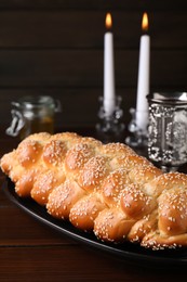 Homemade braided bread with sesame seeds, goblet and candles on wooden table, closeup. Traditional Shabbat challah