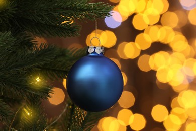 Beautiful blue bauble hanging on Christmas tree against blurred festive lights, closeup