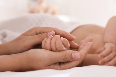 Mother with her cute baby on bed at home, closeup of hands