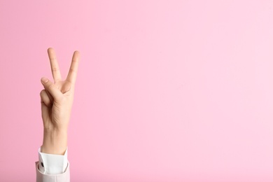 Young woman showing victory gesture on color background. Space for text