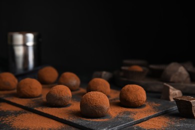 Delicious chocolate truffles powdered with cocoa on black table, space for text
