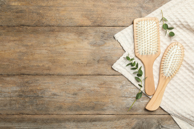 New hair brushes, twigs and towel on wooden background, flat lay. Space for text