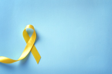 Photo of Yellow ribbon on color background, top view. Cancer awareness