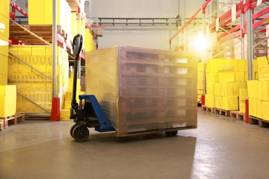 Modern manual forklift with wrapped wooden pallets in warehouse