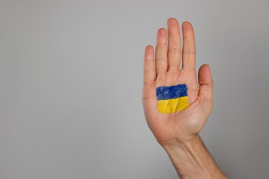 Man with drawing of Ukrainian flag on palm against light grey background, closeup. Space for text