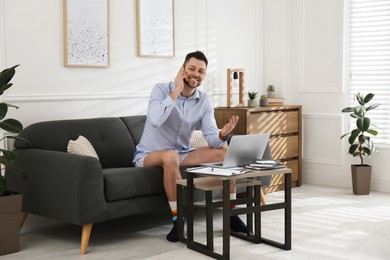 Businessman in shirt and underwear talking on phone while working with laptop at home