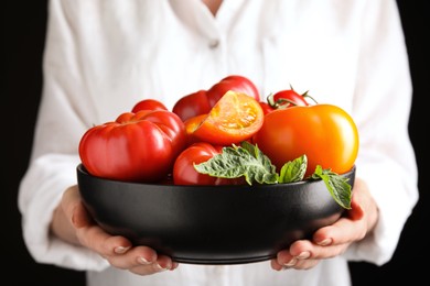 Woman holding bowl with fresh ripe tomatoes on black background, closeup