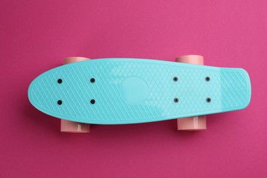 Turquoise skateboard on crimson background, top view