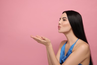 Photo of Beautiful young woman blowing kiss on pink background. Space for text