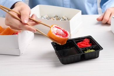 Woman eating sushi rolls with chopsticks at white wooden table, closeup