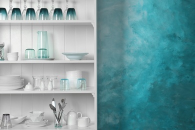 White shelving unit with set of dishware near color wall. Space for text