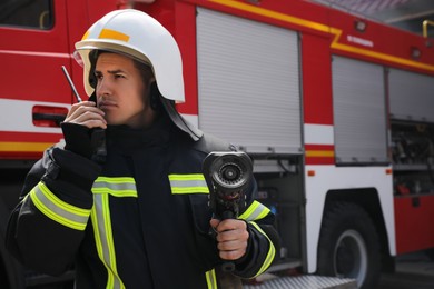 Firefighter with high pressure water jet using portable radio set near fire truck outdoors