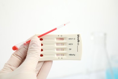 Doctor holding disposable express test for hepatitis and pipette with blood indoors, closeup