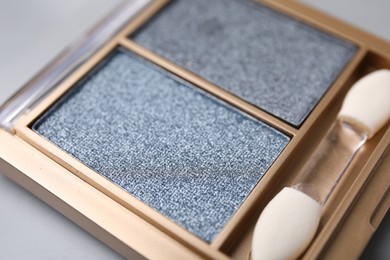Photo of Beautiful eyeshadow palette with applicator on light gray background, closeup. Professional cosmetic product
