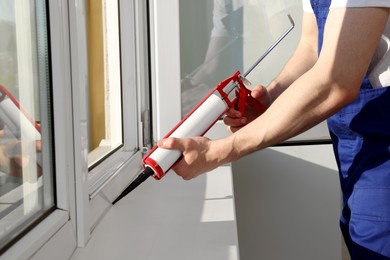 Worker sealing plastic window with caulk indoors, closeup. Installation process