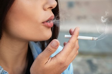 Photo of Young woman smoking cigarette outdoors, closeup view
