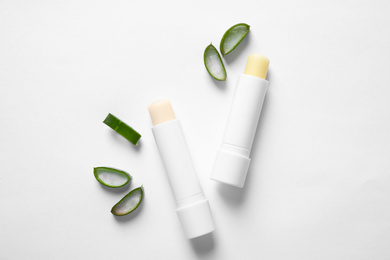 Hygienic lipsticks and cut aloe vera leaf on white background, top view