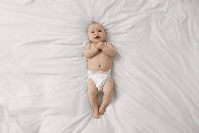 Photo of Cute little baby in diaper lying on white bed, top view