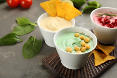 Different kinds of tasty hummus served with nachos on grey table, space for text