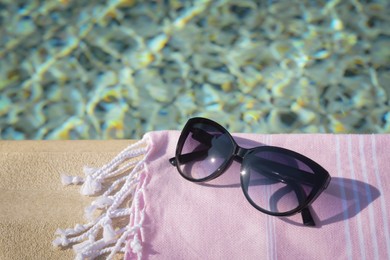 Stylish sunglasses and blanket near outdoor pool on sunny day, space for text