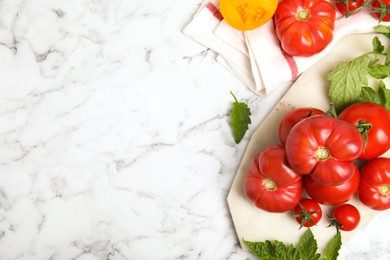 Flat lay composition with different ripe tomatoes and leaves on white marble table. Space for text