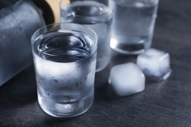 Shot glasses of vodka with ice on dark table, closeup