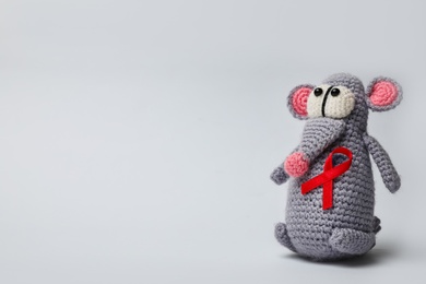 Cute knitted toy mouse with red ribbon on light grey background, space for text. AIDS disease awareness