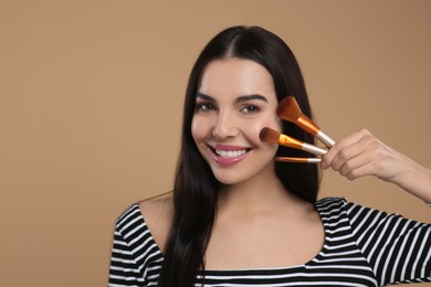 Photo of Happy woman with different makeup brushes on light brown background. Space for text