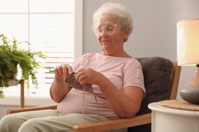 Elderly woman crocheting at home. Creative hobby