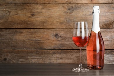 Bottle and glass of delicious rose wine on table against wooden background. Space for text