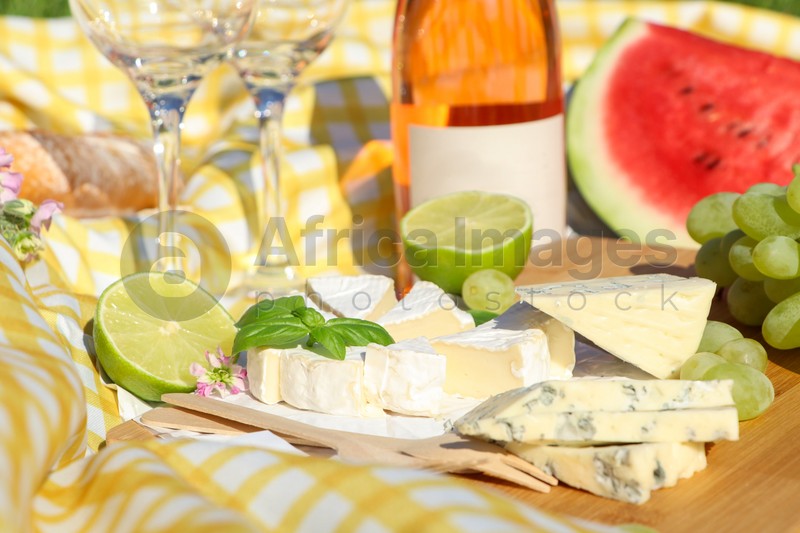 Delicious cheeses with basil and fruits on picnic blanket, closeup
