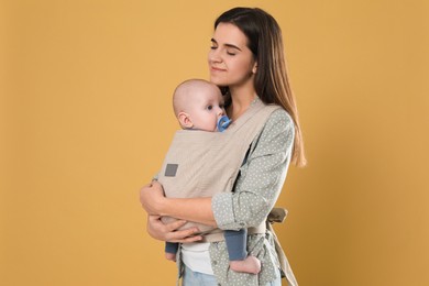Photo of Mother holding her child in sling (baby carrier) on beige background