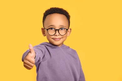 Photo of African-American boy with glasses showing thumb up on yellow background