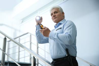 Professional security guard with portable radio set and flashlight on stairs indoors