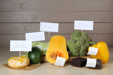 Photo of Food products with calorific value tags on wooden table. Weight loss concept