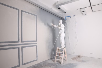 Photo of Decorator dyeing wall in grey color with spray paint indoors