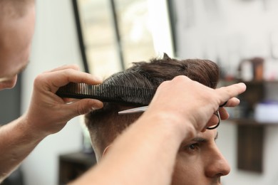 Professional barber making stylish haircut in salon, closeup