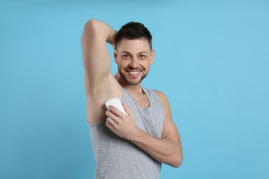 Handsome man applying deodorant on turquoise background