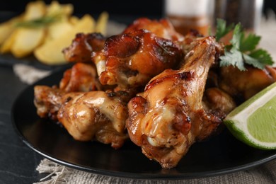 Photo of Delicious fried chicken wings on black plate, closeup