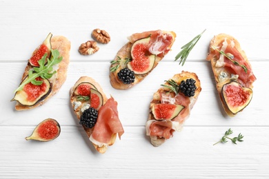Sandwiches with ripe figs and prosciutto served on white wooden table, flat lay
