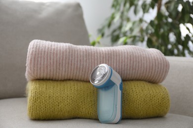 Photo of Modern fabric shaver and woolen sweaters on sofa indoors