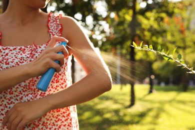 Woman applying insect repellent onto hand in park, closeup. Space for text