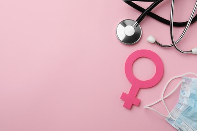 Female gender sign, stethoscope and facial mask on pink background, flat lay. Space for text